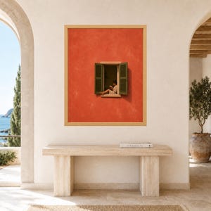 May include: A framed wall art print featuring a vibrant orange textured wall with an open window. The window has dark green shutters and shows a person sitting on the sill reading a book. The artwork is displayed in a light wood frame.