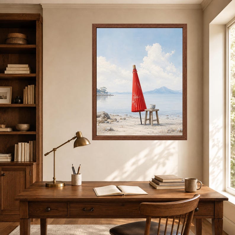 May include: A framed wall art print depicting a bright red traditional Japanese paper umbrella standing upright on a sandy beach next to a small wooden stool, with a calm sea, distant mountains, and a blue sky with white clouds in the background.