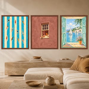 May include: Three framed wall art prints in dark wood frames. The left print shows swimmers in a blue and cream striped pool. The center print depicts a person reading in a window on a terracotta wall. The right print shows a coastal view.