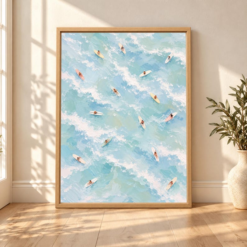 Framed aerial surf wall art showing multiple surfers on pastel surfboards drifting through soft blue ocean waves with white foam in a light textured coastal painting.