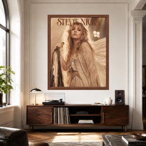 Może przedstawiać: Oprawiony prostokątny wydruk ścienny przedstawiający portret Stevie Nicks w odcieniach sepii z długimi, falowanymi włosami, ubraną w zdobiony koronką str&oacute;j z powiewnymi rękawami, trzymającą mikrofon. Napis STEVIE NICKS jest wydrukowany czcionką szeryfową.