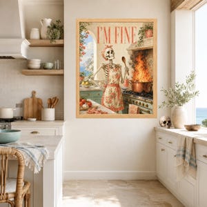 May include: A framed wall art print featuring a skeleton wearing a floral apron and headscarf, standing in a kitchen with a large pot of flames on the stove. The text I'M FINE is printed in red at the top, with a coastal window view in the background.
