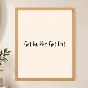 May include: A framed wall art piece featuring a light cream background with the black text Get In, Pee, Get Out. centered in the middle. The artwork is enclosed in a simple, light-toned wooden frame with a clean, rectangular border design.