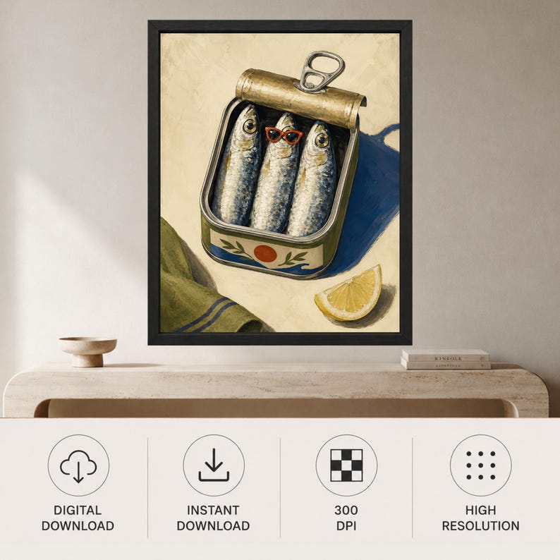 May include: A framed wall art print featuring an open metal tin of three sardines. The center sardine wears small red-rimmed sunglasses. The tin has a green label with a red circle and blue wave design. A lemon wedge sits nearby on a light background.