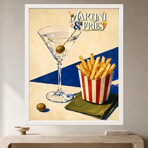 May include: A framed art print featuring a martini glass with an olive, a red and white striped container filled with golden french fries, and a green napkin. The text MARTINI & FRIES is displayed in blue and red script against a cream background.