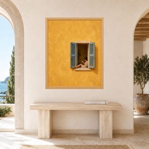 Puede incluir: Una l&aacute;mina de arte enmarcada que muestra una pared de color amarillo mostaza con textura y una ventana central. La ventana tiene contraventanas azules abiertas y muestra a una persona sentada en el alf&eacute;izar leyendo un libro. Marco de madera clara.