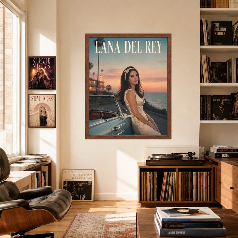 May include: A framed wall poster featuring Lana Del Rey in a white dress leaning against a light blue convertible car at sunset. The text LANA DEL REY is printed in white at the top. The scene includes a coastal road, palm trees, and ocean.