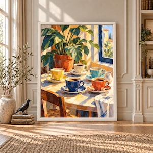 Framed colorful coffee wall art showing five bright coffee cups on a sunlit table beside a large green houseplant and open window in a warm Mediterranean-inspired interior.