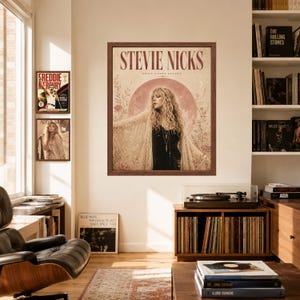 May include: A framed wall poster featuring a portrait of Stevie Nicks with long wavy hair, wearing a dark top and a lace shawl. The background includes a large pink moon, floral illustrations, and the text STEVIE NICKS BELLA DONNA DREAMS.