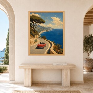 May include: A framed vertical wall art print depicting a red convertible car driving along a winding coastal road. The scene features a deep blue sea, rocky cliffs, green trees, and a bright sky with white clouds, all captured in a painterly style.