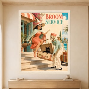 Framed Broom Service wall art showing a retro witch sitting on a broom beside a skeleton hotel bellhop carrying an open suitcase with a black cat inside at a sunny seaside resort.