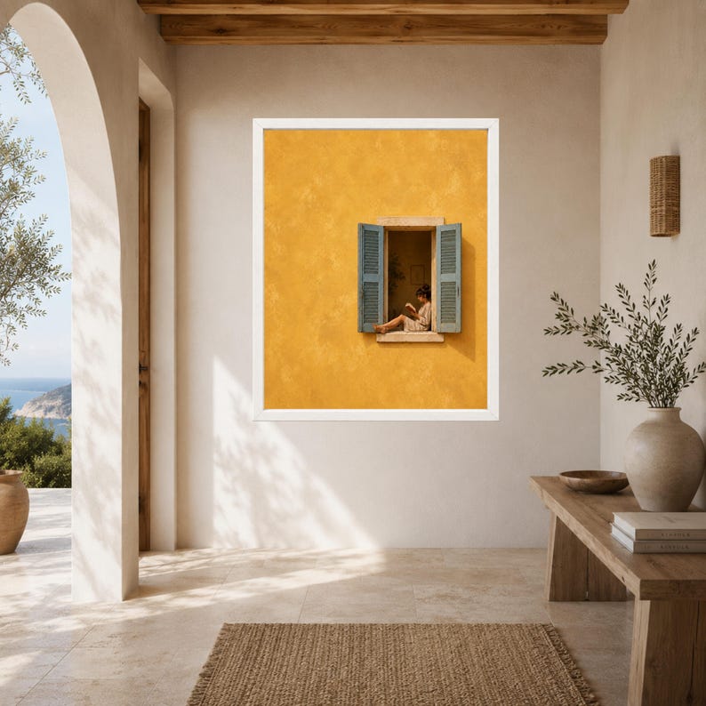 Puede incluir: Una impresi&oacute;n de arte mural enmarcada que muestra una pared de color amarillo mostaza con textura y una ventana abierta. La ventana tiene contraventanas de color azul claro y muestra a una persona sentada leyendo un libro. Marco blanco.