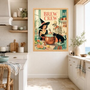 May include: A framed wall art print titled BREW CREW featuring a witch in a black hat, a skeleton wearing a red bowtie, and a black cat gathered around a copper cauldron. The illustration includes citrus fruits, glassware, and kitchen elements.