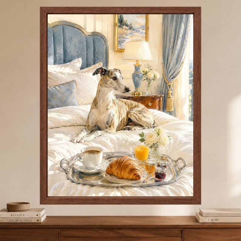 May include: A framed wall art print featuring a brindle greyhound resting on a white bedspread. A silver tray sits on the bed, holding a white coffee cup, a croissant, a glass of orange juice, and small jars of jam, with a blue headboard behind.