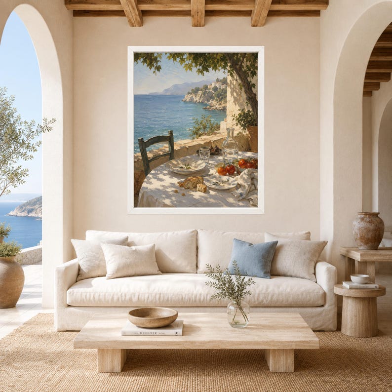 May include: A framed wall art print depicting a coastal scene with a table set for a meal on a terrace overlooking the sea. The painting features a white tablecloth, plates, a glass bottle, and tomatoes under the shade of a tree branch.
