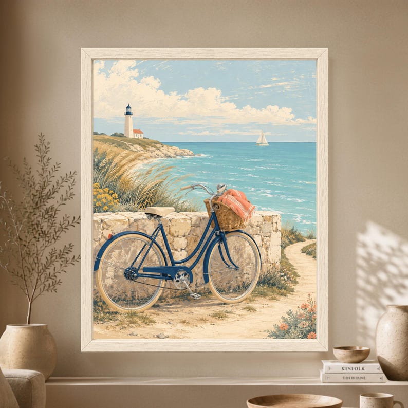 Framed coastal wall art showing a blue vintage bicycle with a wicker basket and coral blanket beside turquoise ocean water, with a white lighthouse and sailboat in the distance.