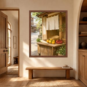 Puede incluir: Una impresi&oacute;n art&iacute;stica enmarcada que representa un puesto de madera en una calle soleada. El puesto cuenta con una cortina noren blanca, un r&aacute;bano daikon, varias frutas c&iacute;tricas amarillas, una cesta de mimbre y un fardo de tela roja sobre una superficie de madera r&uacute;stica.