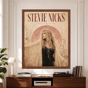 Framed Stevie Nicks wall art with a female rock singer in a black dress and cream lace shawl, surrounded by muted pink flowers, stars and a crescent moon on an aged beige background.