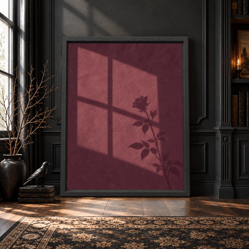 Framed burgundy botanical wall art showing the shadow of a single rose and leaves beneath a large window shadow across a textured wine red wall.