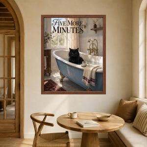 May include: A framed wall art print featuring a black cat sitting in a blue clawfoot bathtub filled with water. The text 'FIVE MORE MINUTES' is printed at the top. A white towel hangs over the edge of the tub next to a small cup and saucer.