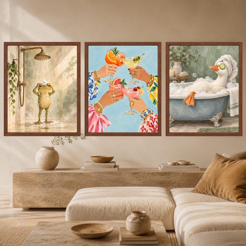 May include: A set of three framed wall art prints. The left print shows a frog showering. The center print depicts four hands holding colorful cocktails with fruit garnishes. The right print features a white duck in a bubble bath with cucumber slices.