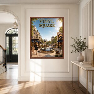 May include: A rectangular framed wall art print featuring a European-style town square with a central fountain, people walking, and the text VINYL SQUARE in gold lettering at the top. The scene depicts buildings, trees, and a clear blue sky.
