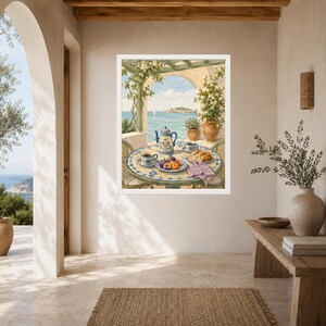 May include: A framed wall art print depicting a Mediterranean terrace scene with a round tiled table set for breakfast. The table features a blue and white teapot, cups, a plate of fresh fruit, and a pastry, overlooking a calm blue sea.