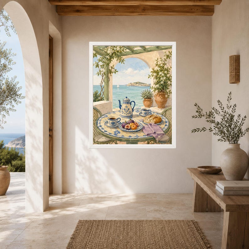May include: A framed wall art print depicting a Mediterranean terrace scene with a round tiled table set for breakfast. The table features a blue and white teapot, cups, a plate of fresh fruit, and a pastry, overlooking a calm blue sea.