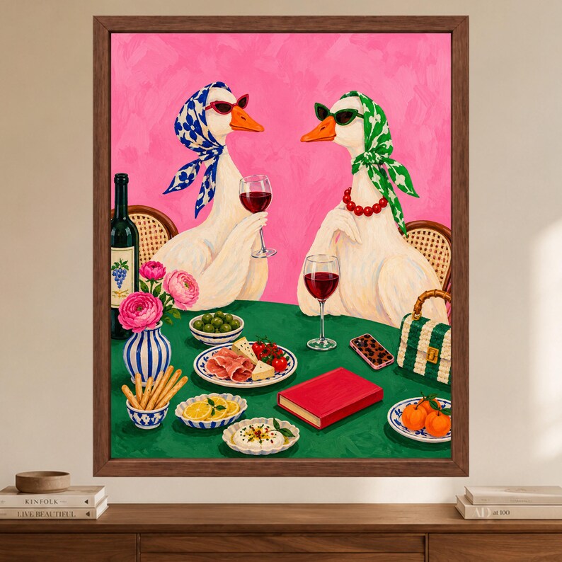May include: A framed painting depicts two white geese wearing headscarves and sunglasses, sitting at a green table with wine glasses, a bottle of wine, a vase of pink flowers, plates of food, a red book, a smartphone, and a small handbag.