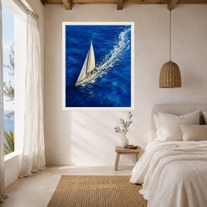 May include: A framed wall art print featuring an aerial view of a white sailboat gliding across deep blue ocean water, creating a white wake behind it. The sailboat has a single tall mast and a triangular sail, captured from a high angle.