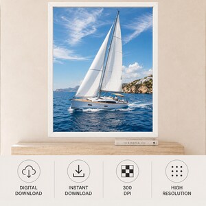 Puede incluir: Una impresi&oacute;n de arte mural enmarcada que muestra un velero blanco con velas desplegadas navegando en aguas oce&aacute;nicas azul profundo bajo un cielo brillante con nubes tenues. Incluye una costa rocosa con edificios blancos y el libro The Kinfolk Home.