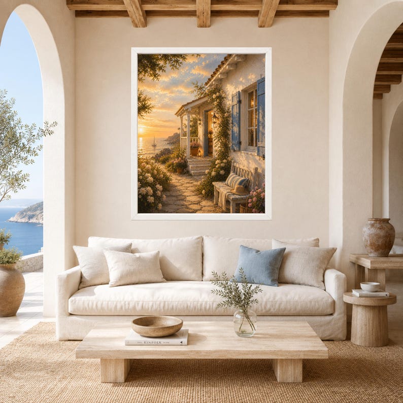 May include: A framed wall art print depicting a Mediterranean-style cottage at sunset, featuring a stone path, climbing vines, blue shutters, and a wooden bench. The scene includes a coastal view with a sailboat on the water under a golden sky.