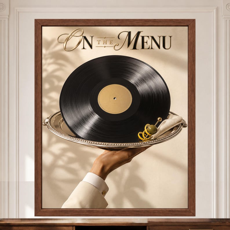 May include: A framed wall art print featuring a black vinyl record served on a silver platter with a green olive garnish. The text "On the Menu" is printed in elegant gold lettering at the top. The composition is set against a neutral background.