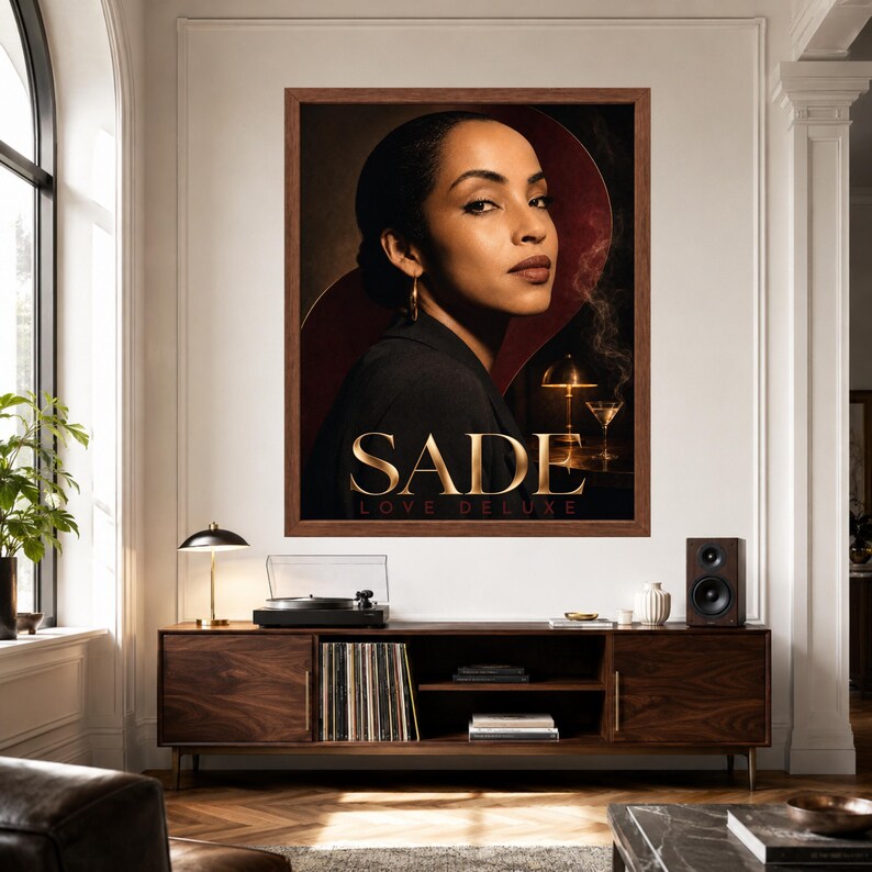 K&ouml;nnte beinhalten: Ein gerahmtes Wandposter mit einem Portr&auml;t von Sade und dem Text SADE LOVE DELUXE. Das Kunstwerk zeigt eine Person in einem dunklen Blazer vor einem dunklen Hintergrund mit einer leuchtenden Lampe und einem Martiniglas. Das Poster h&auml;ngt an einer wei&szlig;en Wand.