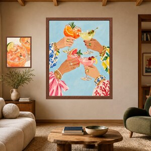 May include: A framed wall art print depicting four hands raised in a toast, each holding a different cocktail glass filled with colorful drinks garnished with fruit slices, olives, and cherries, set against a light blue background.