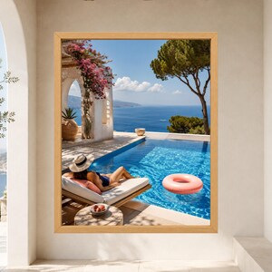 May include: A framed wall art print depicting a Mediterranean scene with a person in a sun hat lounging on a poolside daybed. The view features a bright blue swimming pool, a pink inflatable ring, a stone archway with bougainvillea, and the sea.
