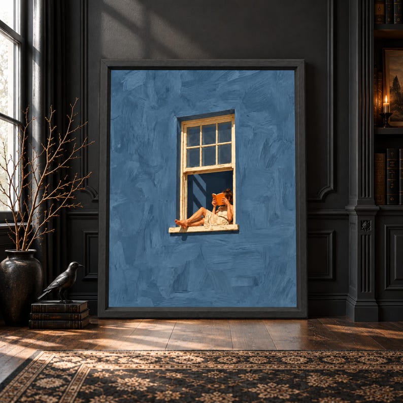 Framed dusty blue wall art showing a barefoot woman sitting in a small open window reading an orange book against a large textured muted blue facade.