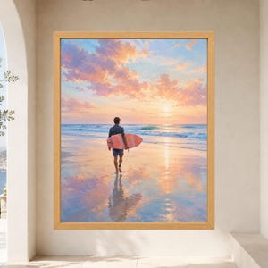 May include: A framed wall art print featuring a person walking on a wet sandy beach at sunset while carrying a coral-colored surfboard. The sky is filled with soft pink and orange clouds reflecting on the water and the wet sand below.