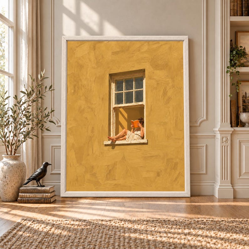Framed mustard yellow wall art showing a barefoot woman sitting in an open cream window while reading an orange book against a textured warm yellow wall.