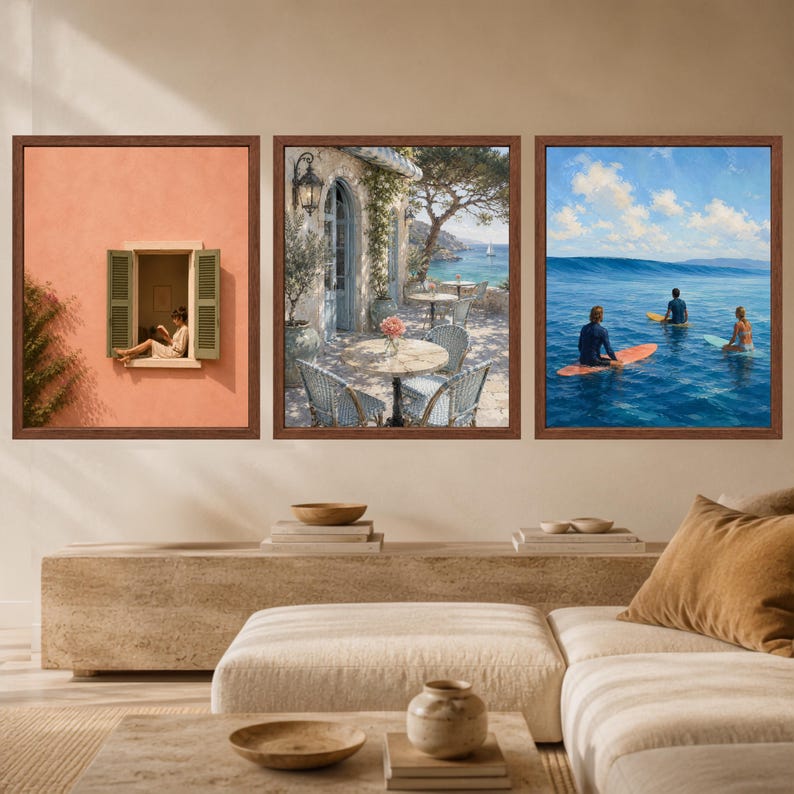 May include: A set of three framed wall art prints featuring a person sitting in a peach-colored window, a Mediterranean seaside patio with tables and chairs, and three surfers on blue ocean waves under a bright sky with white clouds.