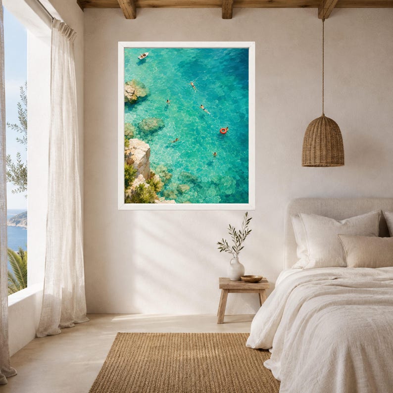 Puede incluir: Una impresi&oacute;n de arte mural enmarcada que muestra una vista a&eacute;rea de aguas costeras turquesas con acantilados rocosos, varios nadadores y un peque&ntilde;o barco. La escena incluye un anillo flotador circular de color rojo brillante en el agua clara.