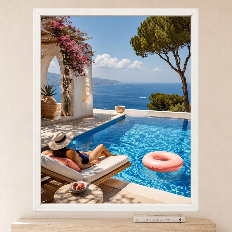 May include: A framed wall art print depicting a person in a sun hat and swimsuit lounging on a white cushioned deck chair beside a blue swimming pool. A pink inflatable ring floats in the water, with a stone archway, pink flowers, and sea view.