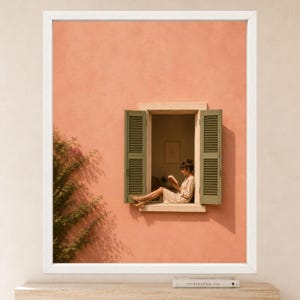 May include: A framed wall art print featuring a peach-colored stucco wall with a window. The window has open green shutters and a person sitting inside reading a book. A green climbing plant grows along the left side of the textured wall surface.