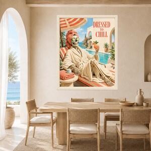 May include: A framed wall art print featuring a skeleton wearing a beige bathrobe, a matching head towel, and cucumber slices over its eyes. The skeleton reclines on a lounge chair by a pool, holding a cocktail, with the text DRESSED TO CHILL.