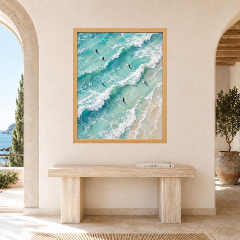 May include: A framed wall art print featuring an aerial view of turquoise ocean waves crashing onto a sandy beach. Several surfers are positioned on their boards in the water, surrounded by white sea foam and varying shades of blue water.