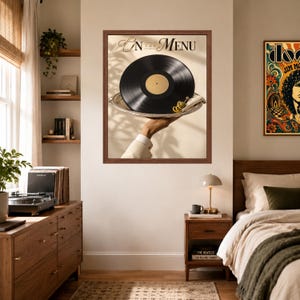 May include: A framed wall art print titled On The Menu featuring a black vinyl record with a gold center label resting on a silver serving tray. A green olive garnish sits on the tray edge. The print is displayed in a dark brown wooden frame.