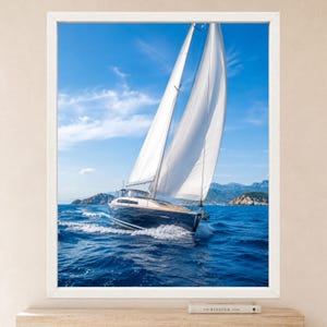 Op de afbeelding: Een ingelijste wandkunstprint met een donkerblauw zeiljacht met witte zeilen dat door diepblauw oceaanwater vaart onder een heldere lucht met lichte wolken, met verre rotsachtige eilanden zichtbaar op de horizonlijn op de achtergrond.
