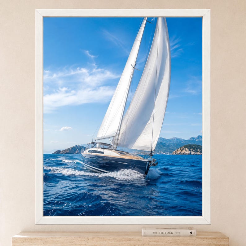 Op de afbeelding: Een ingelijste wandkunstprint met een donkerblauw zeiljacht met witte zeilen dat door diepblauw oceaanwater vaart onder een heldere lucht met lichte wolken, met verre rotsachtige eilanden zichtbaar op de horizonlijn op de achtergrond.