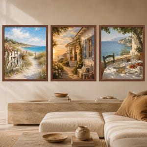 May include: A set of three framed wall art prints featuring coastal scenes. The left print shows a bicycle on a sandy path by the sea. The center print depicts a cottage at sunset. The right print displays a table set for a meal overlooking the ocean.