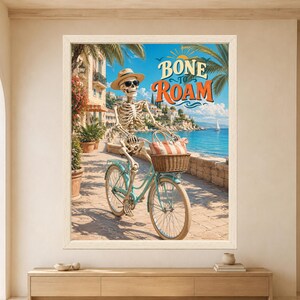 Peut inclure: Une impression d'art encadr&eacute;e repr&eacute;sentant un squelette portant un chapeau beige et des lunettes de soleil, sur un v&eacute;lo bleu clair avec un panier en osier contenant un sac ray&eacute; rouge et blanc. Le texte BONE TO ROAM est &eacute;crit en orange et bleu.